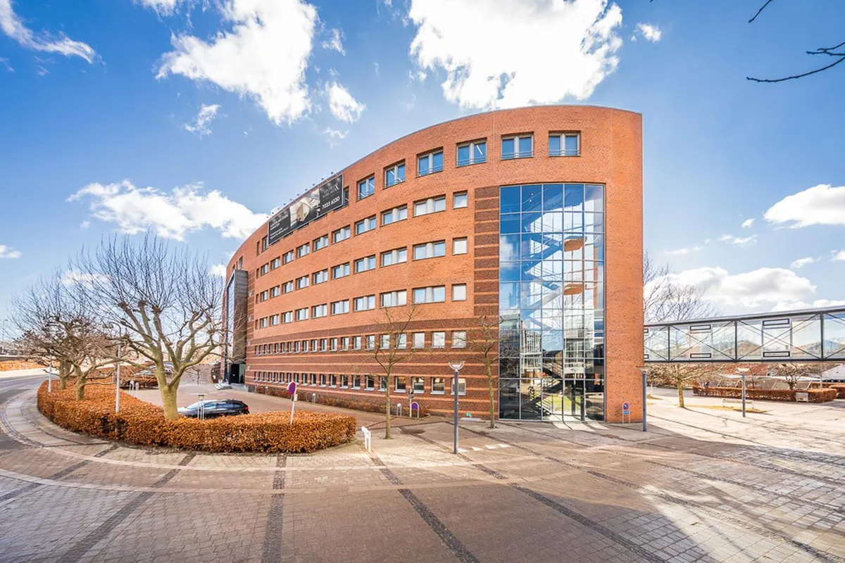 Moderne kontorbygning med gul tegl og glasvinduer i Kongens Lyngby, parkeringsplads og gåbro