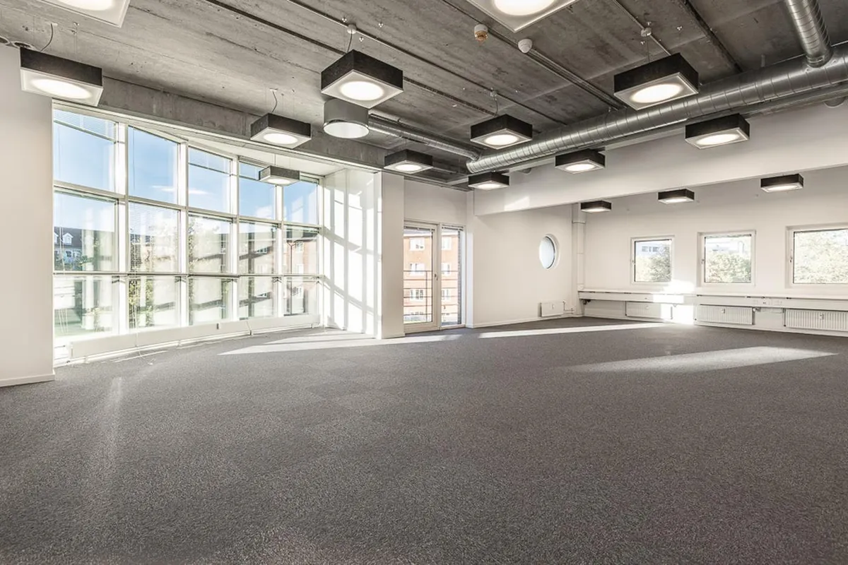 Kontorlokale med hvide vægge, gulvtæppe og store vinduer, lysekroner og runde vinduer, lyse og rummelige.