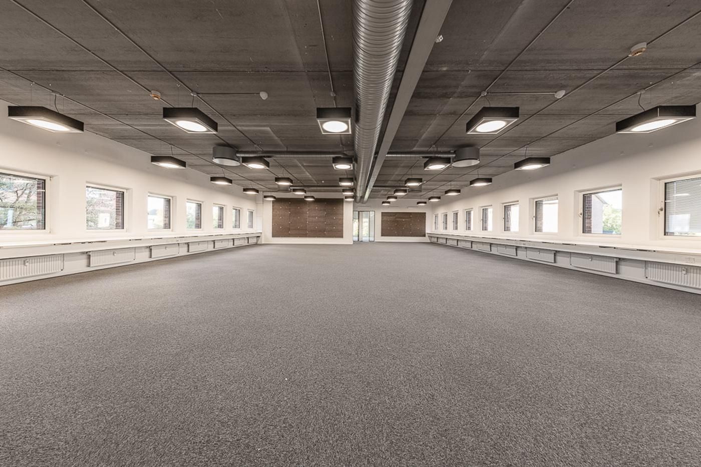 Et stort og lyse kontor med hvide vægge, grå gulv og store vinduer langs væggen. Loftet er lavt og er udstyret med flere