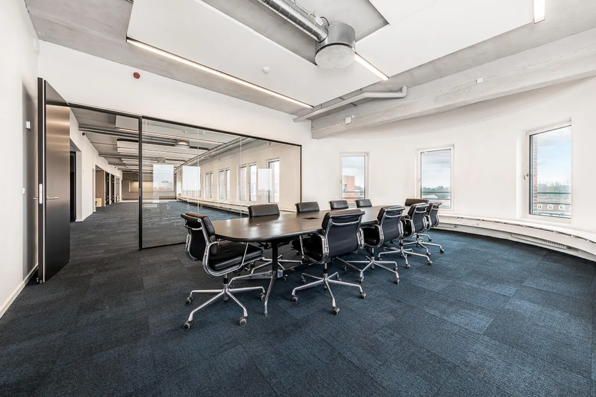 Et stort mødelokale med moderne interiør og en stor gulvbelægning og lange vinduer