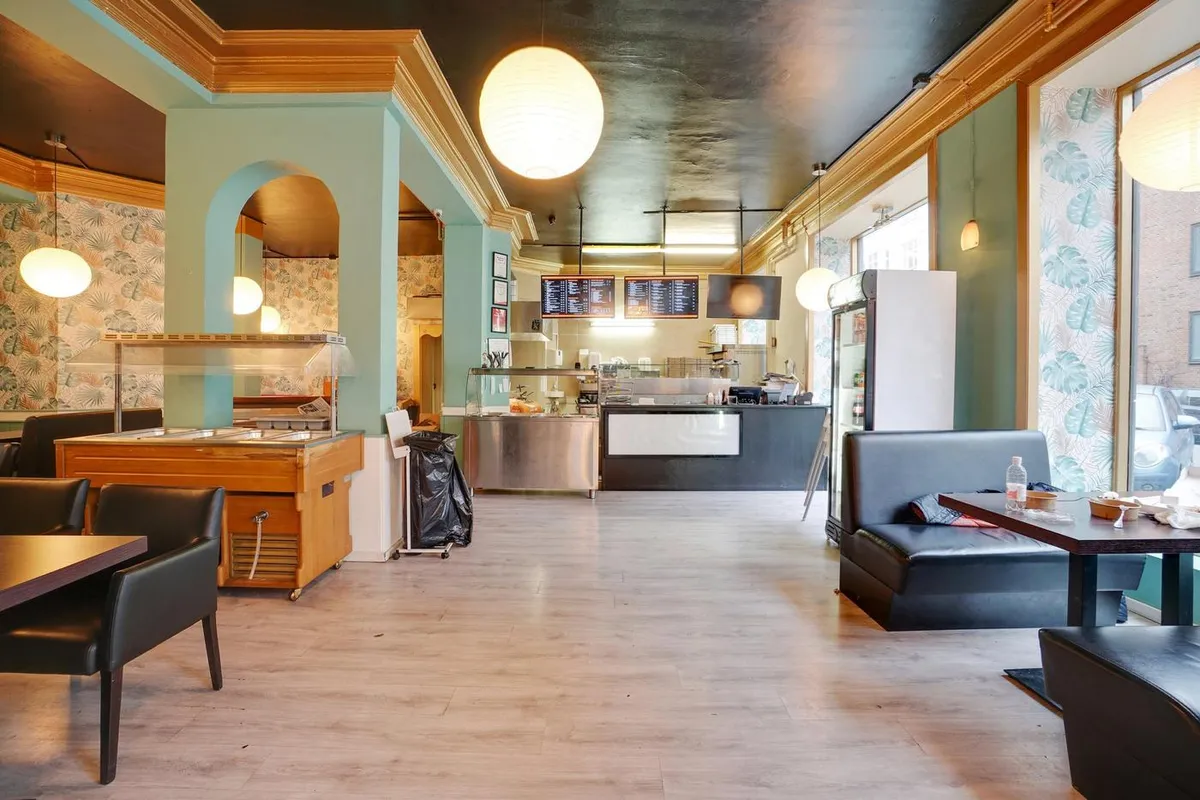 Erhvervsandel med hjørnebeliggenhed i hjertet af Nørrebro med moderne interiør og trægulv, lyse loftslampe og bord med en