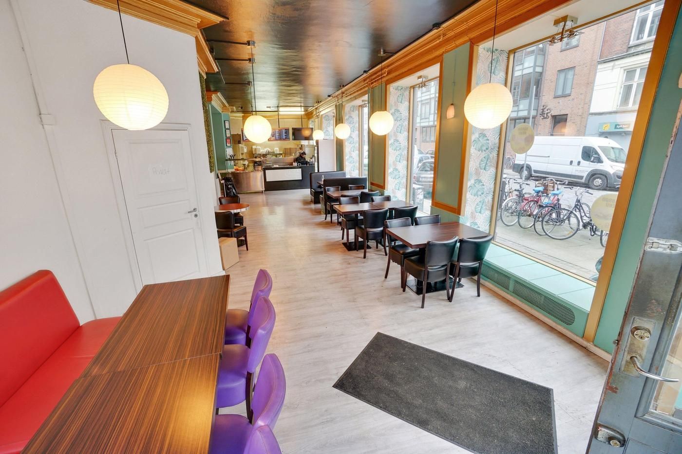 En moderne café med lyse loftslamper og runde lampekugler samt røde og lilla stole og borde