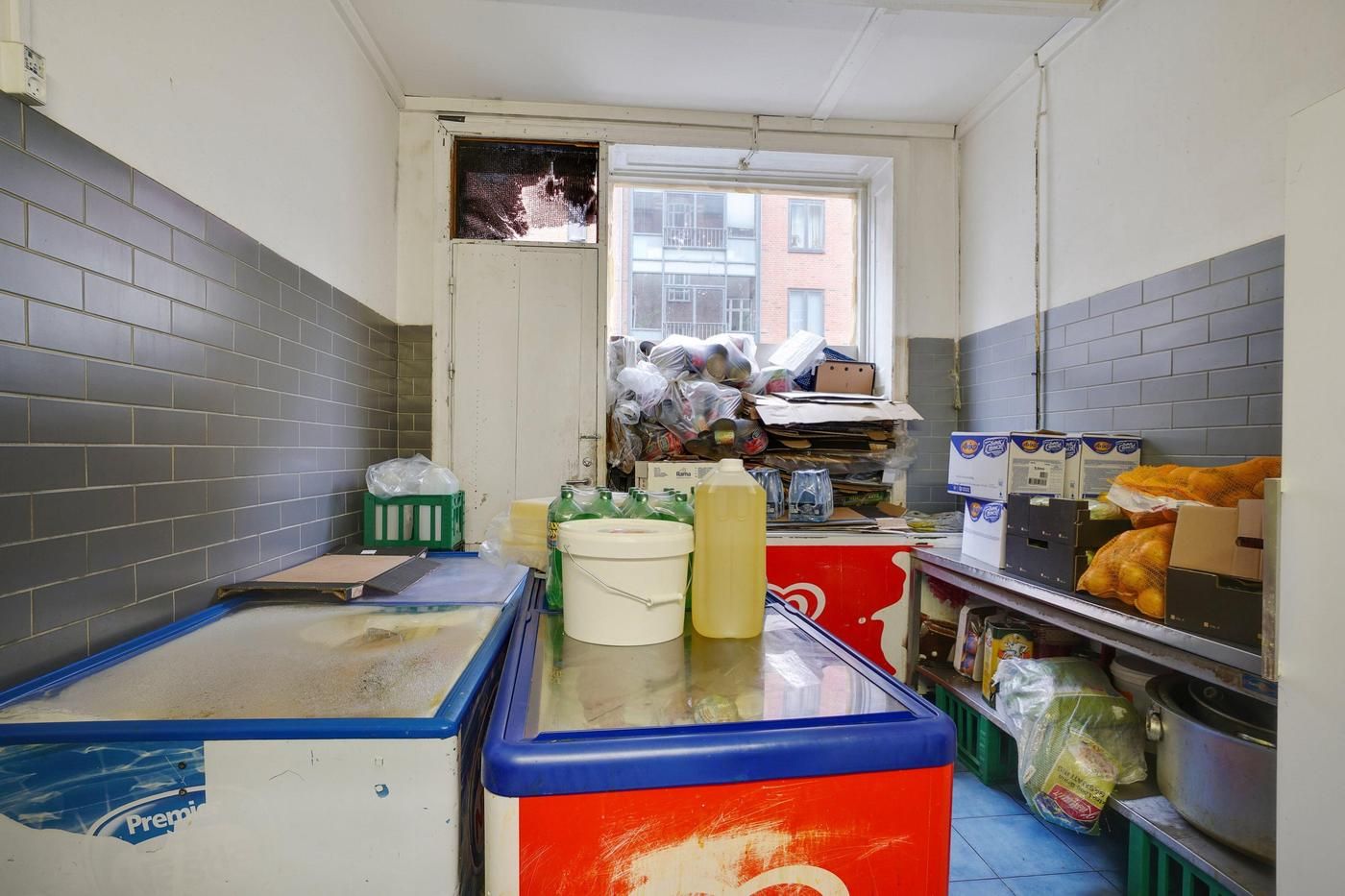 En kombineret køkken og opbevaringsrum med køleskabe, beholdere, plastposer og kasserne med forskellige produkter samt et