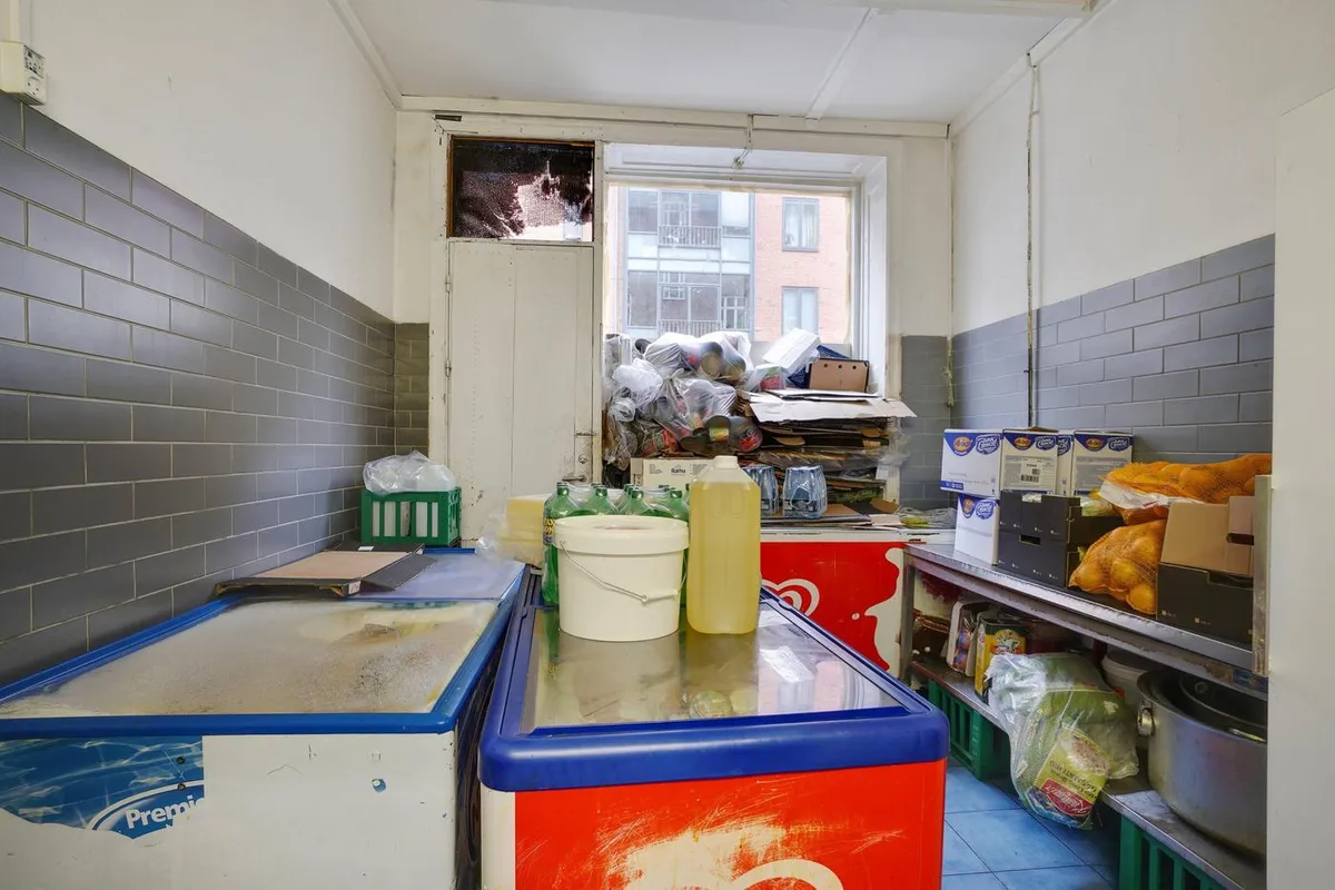 En kombineret køkken og opbevaringsrum med køleskabe, beholdere, plastposer og kasserne med forskellige produkter samt et