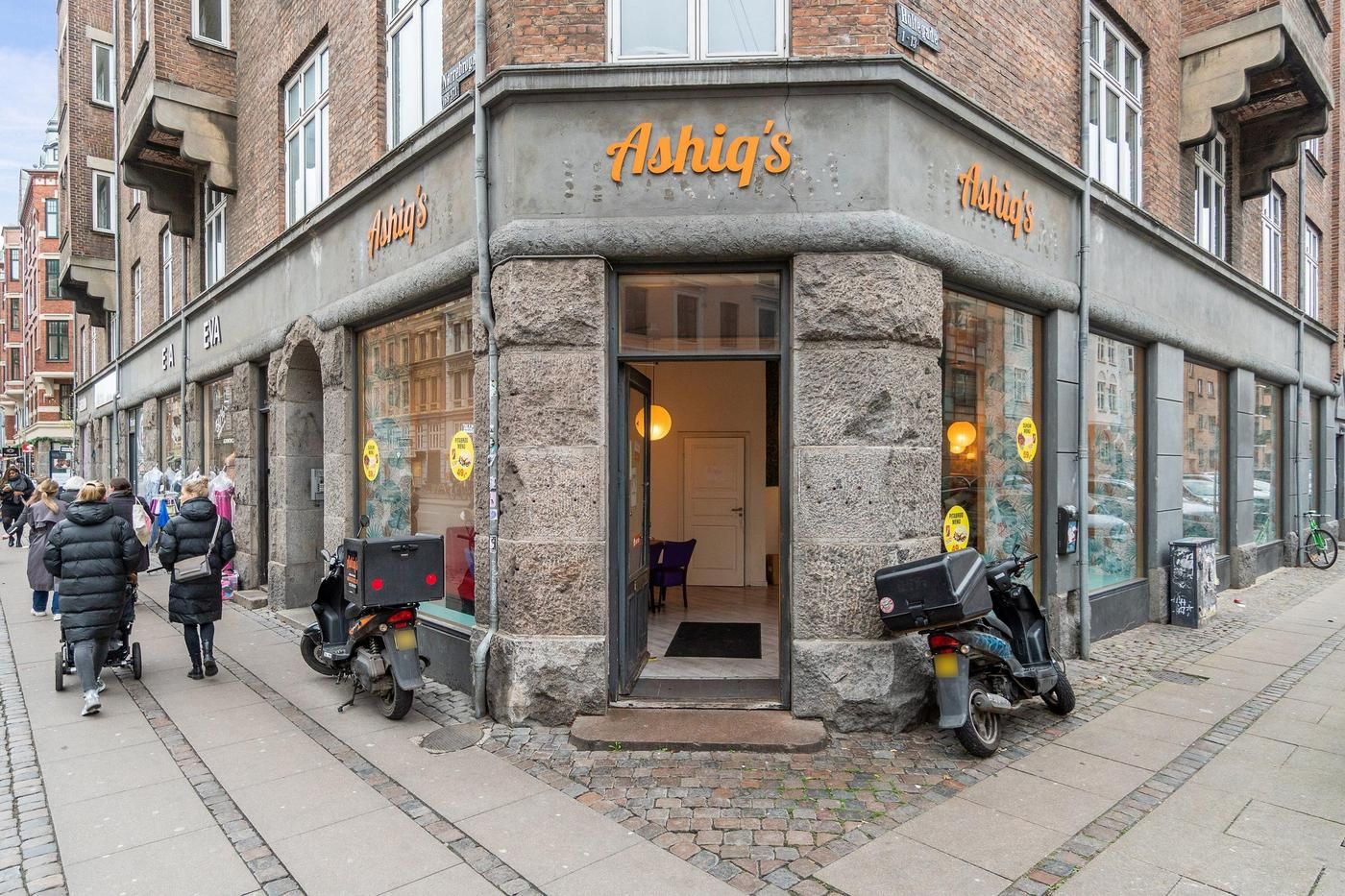 Erhvervsandel med hjørnebeliggenhed i Nørrebro. Hjørnebygning med vinduer og "Ashiiq's" skrift. Parkerede scooterer og
