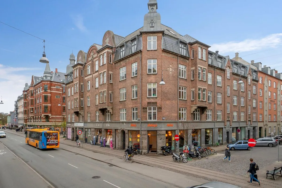 Hjørnebygning med butikker og cyklister på Nørrebrogade, tæt ved Holtegade i København