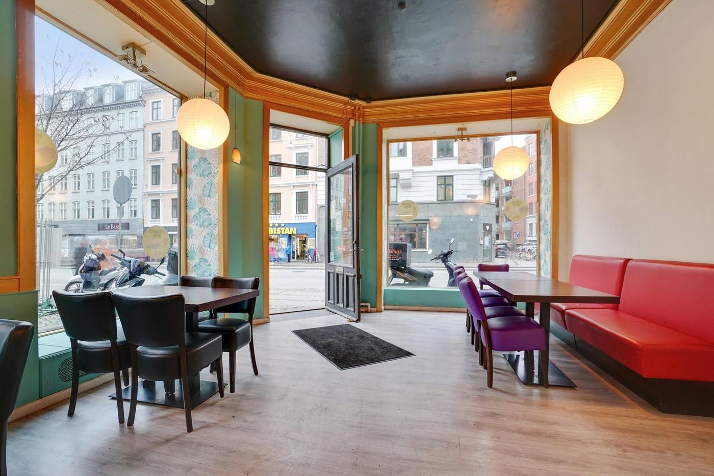 Elegant restaurant med lyse trægulve og grønne vægge. Lyskroner og røde lædersædebanke med runde borde og stole. Åbent