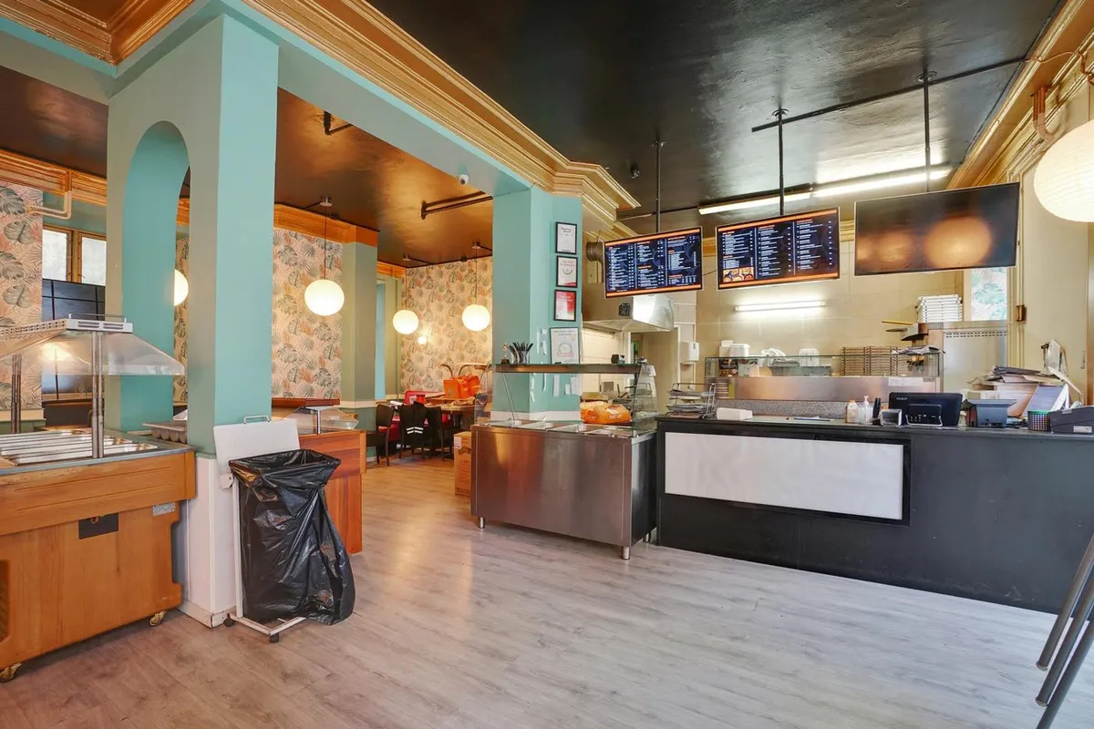 Indvendigt af et kafé med servitre, stole, og en disk. På disken er der en menu, og der er en køkkenudgang. Der er et skab