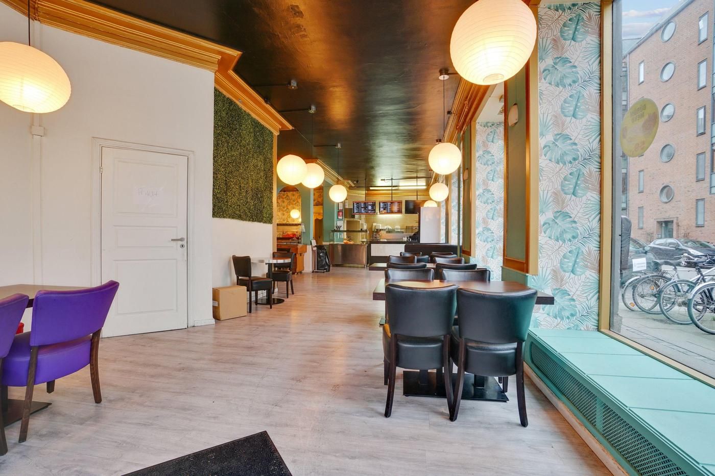 Lyst og moderne café med møbler og lyse gardiner i en bygning med store vinduer