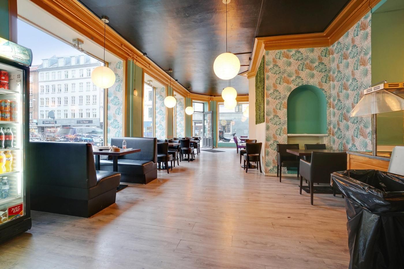 Indvendigt set på et tomt restaurant med lyse lamper og lysegule vægge med grønne mønstre. Sofaer og spiseborde med stole er