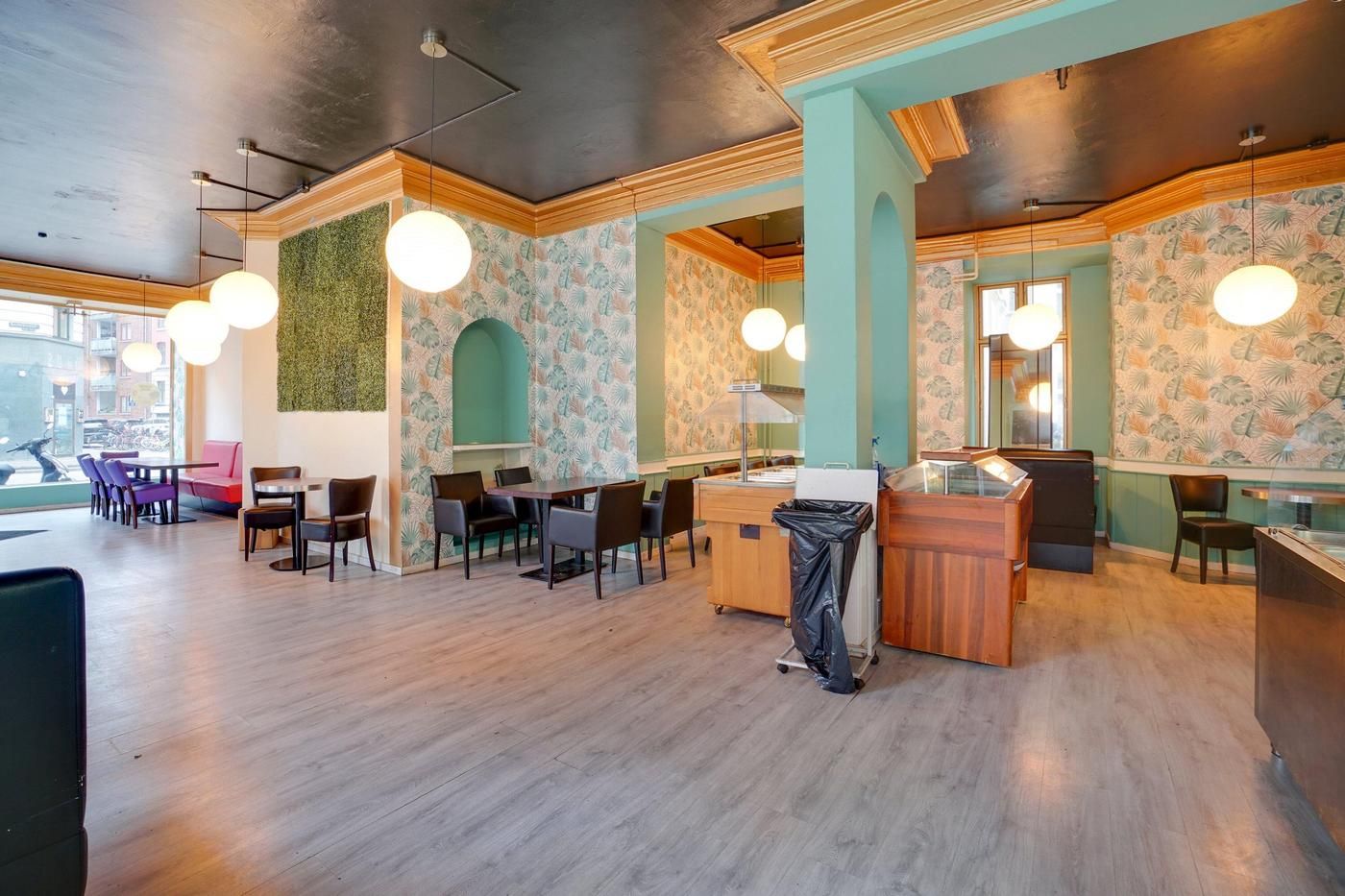 En hyggelig restaurant med trægulve, runde lysekroner, smukt møblerede bord og stole samt en åben udsigt til gaden