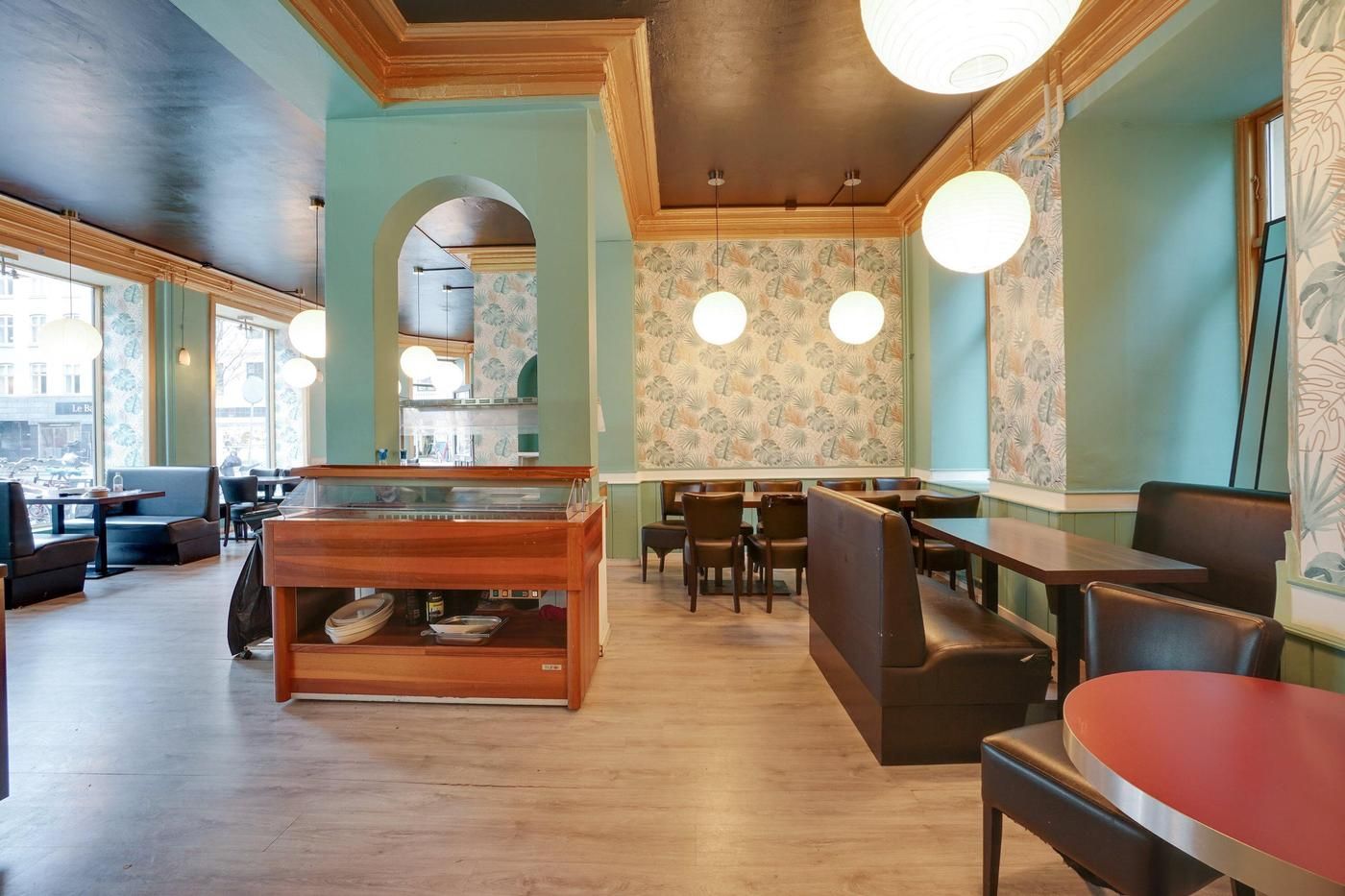 Inde i restauranten med lyseblå vægge, lysekroner, røde og brune borde, og stole samt en glaskabinet med tallerkener