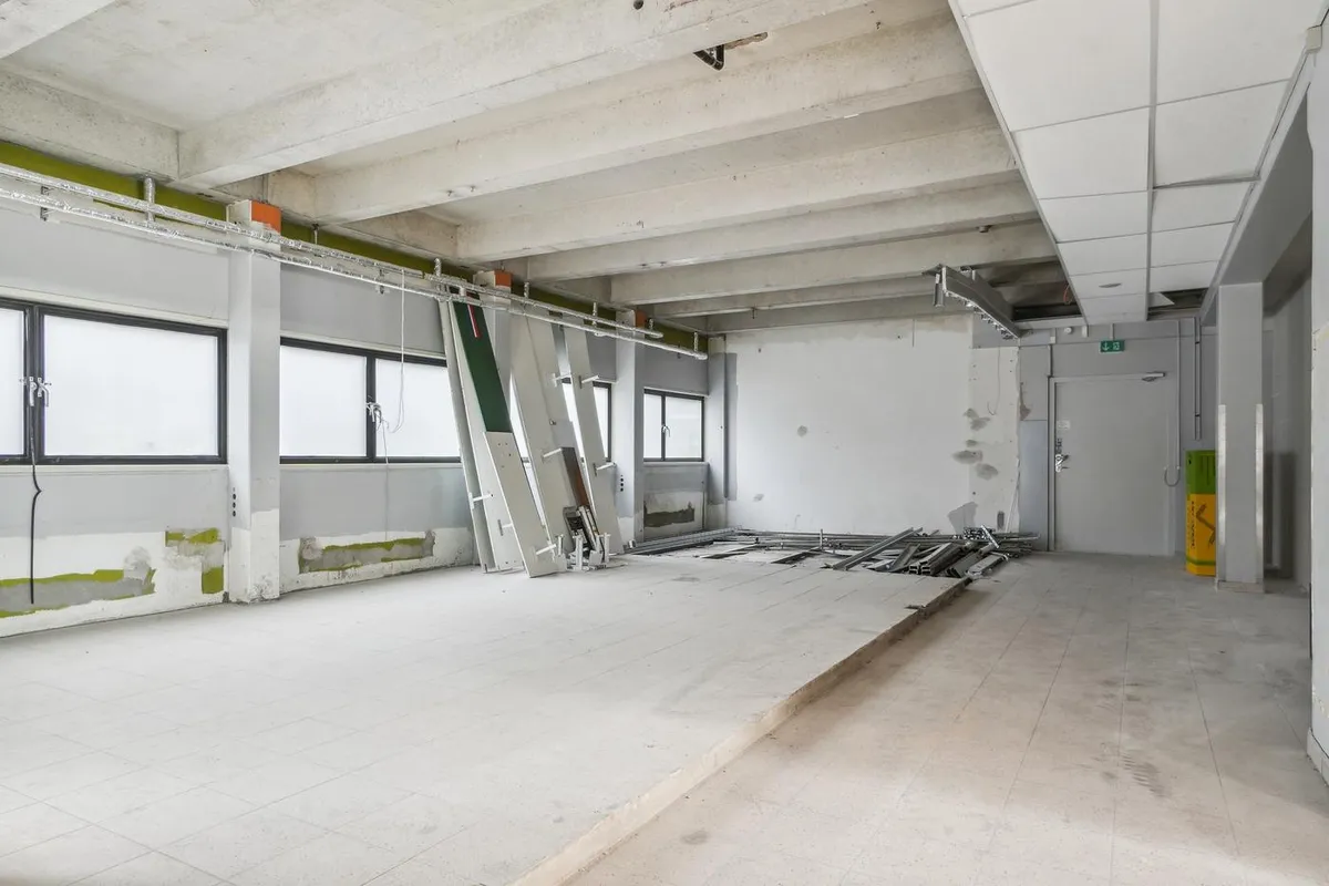 Til renovering: tomt rum med hvide vægge og lofter, store vinduer, stakkelsgulve, røre og skraldespande