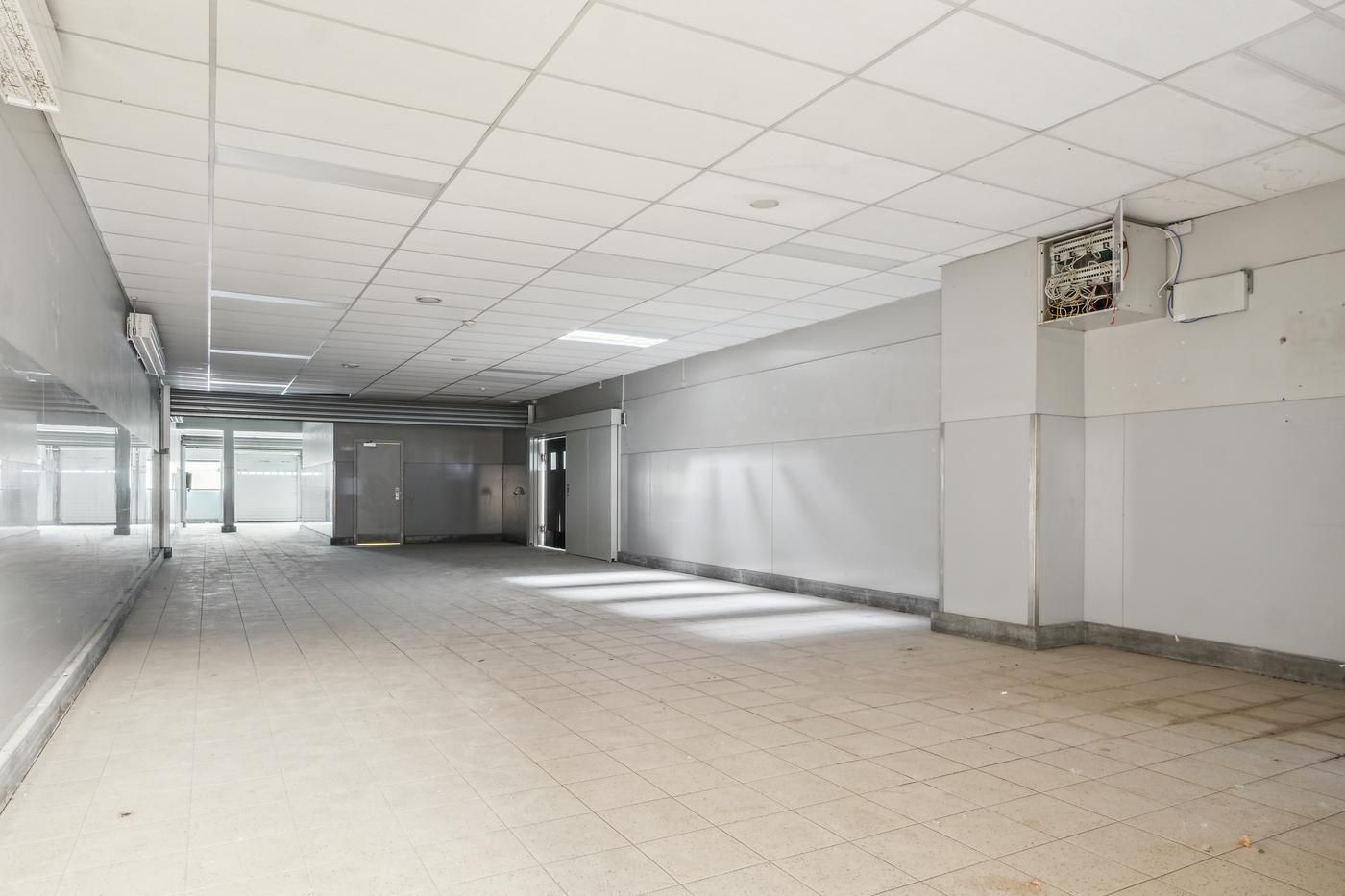 En stor tom gang med hvide vægge og gulvtæppe samt to store indgange til venstre og et elektronisk kontrolpanel til højre