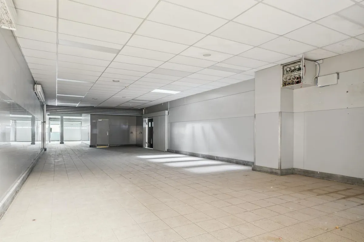 En stor tom gang med hvide vægge og gulvtæppe samt to store indgange til venstre og et elektronisk kontrolpanel til højre