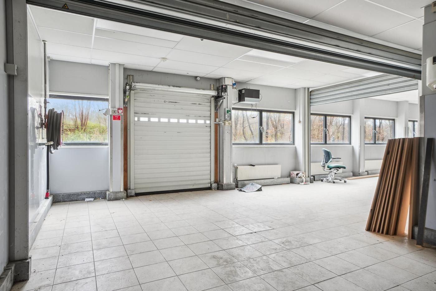 Ledig lagerrum med lukket garagedør og vindue, to stolpemonterede radiatorer, en stol og højt træstapel