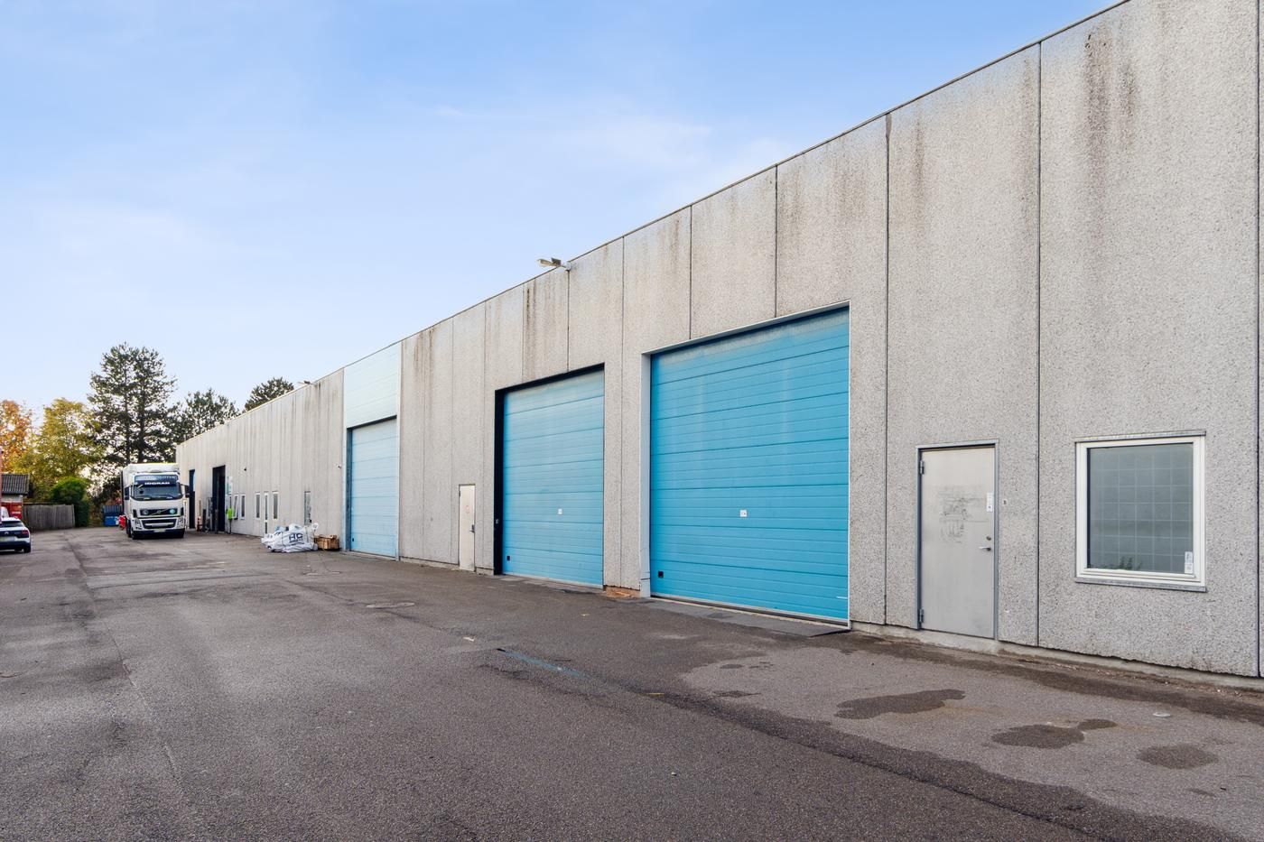 En stor grå bygning med flere blå køretøjsgarager og glasruder i en stille vej i et industriområde