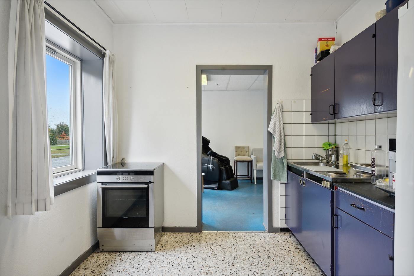 En køkken med et ovn og en sæbeholder samt en køleskab og en stol i en anden rum.