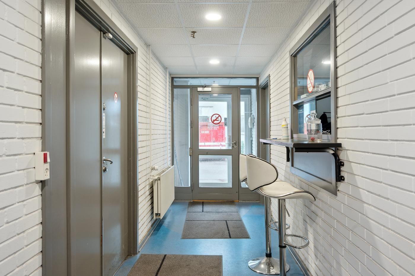 Lager og kontorlokaler med store vinduer og lyse lofter i Glostrup. To høje, hvide, glasdøre og en lille stol med en høj,