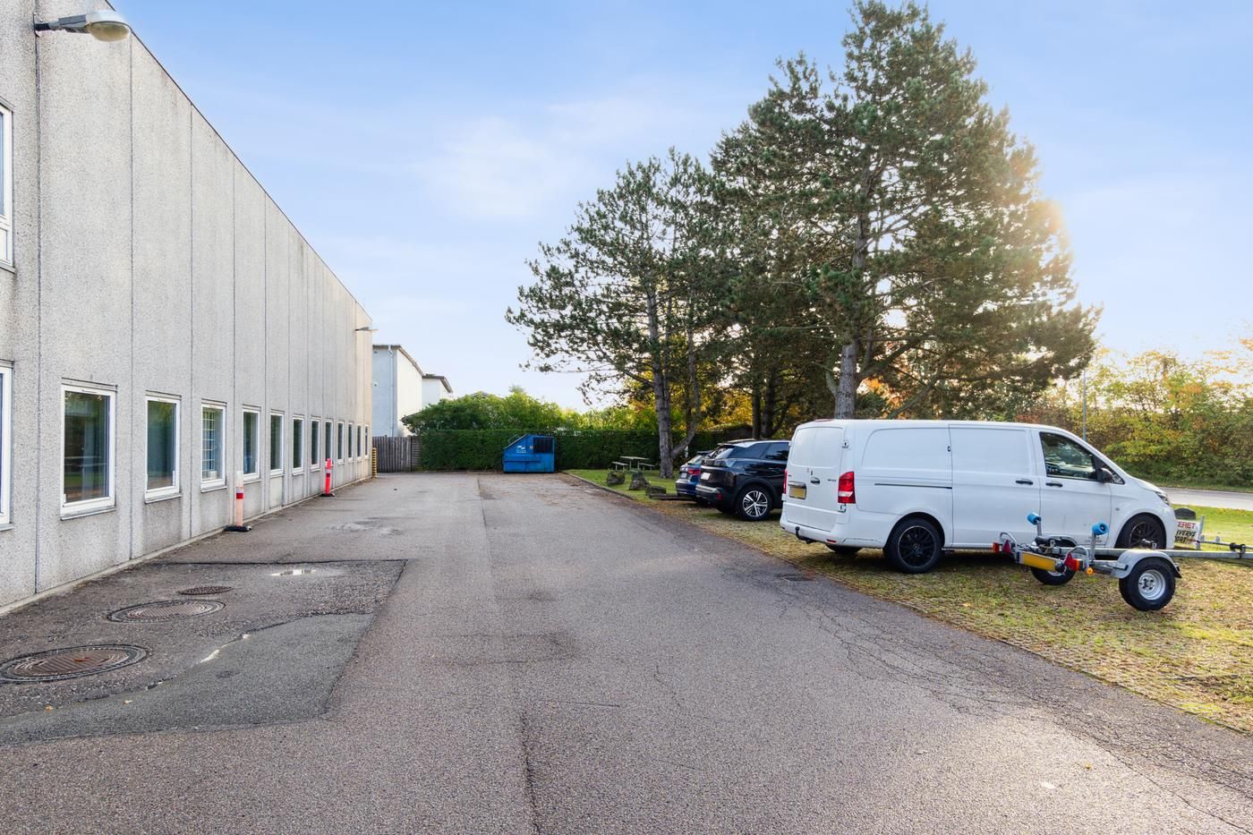 Lagerlejemål med parkeringsplads i roområde. Et hvidt lagerbygning med mange vinduer og en række parkerede biler og en