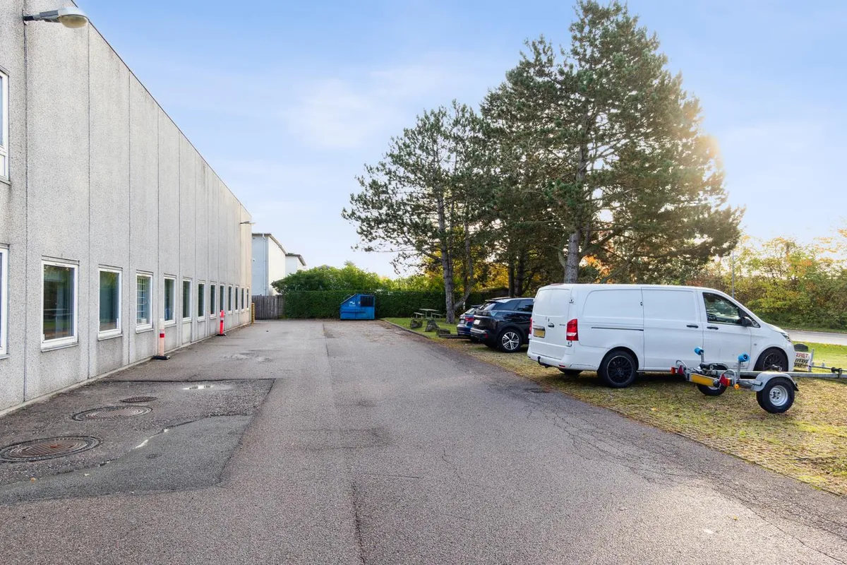 Lagerlejemål med parkeringsplads i roområde. Et hvidt lagerbygning med mange vinduer og en række parkerede biler og en