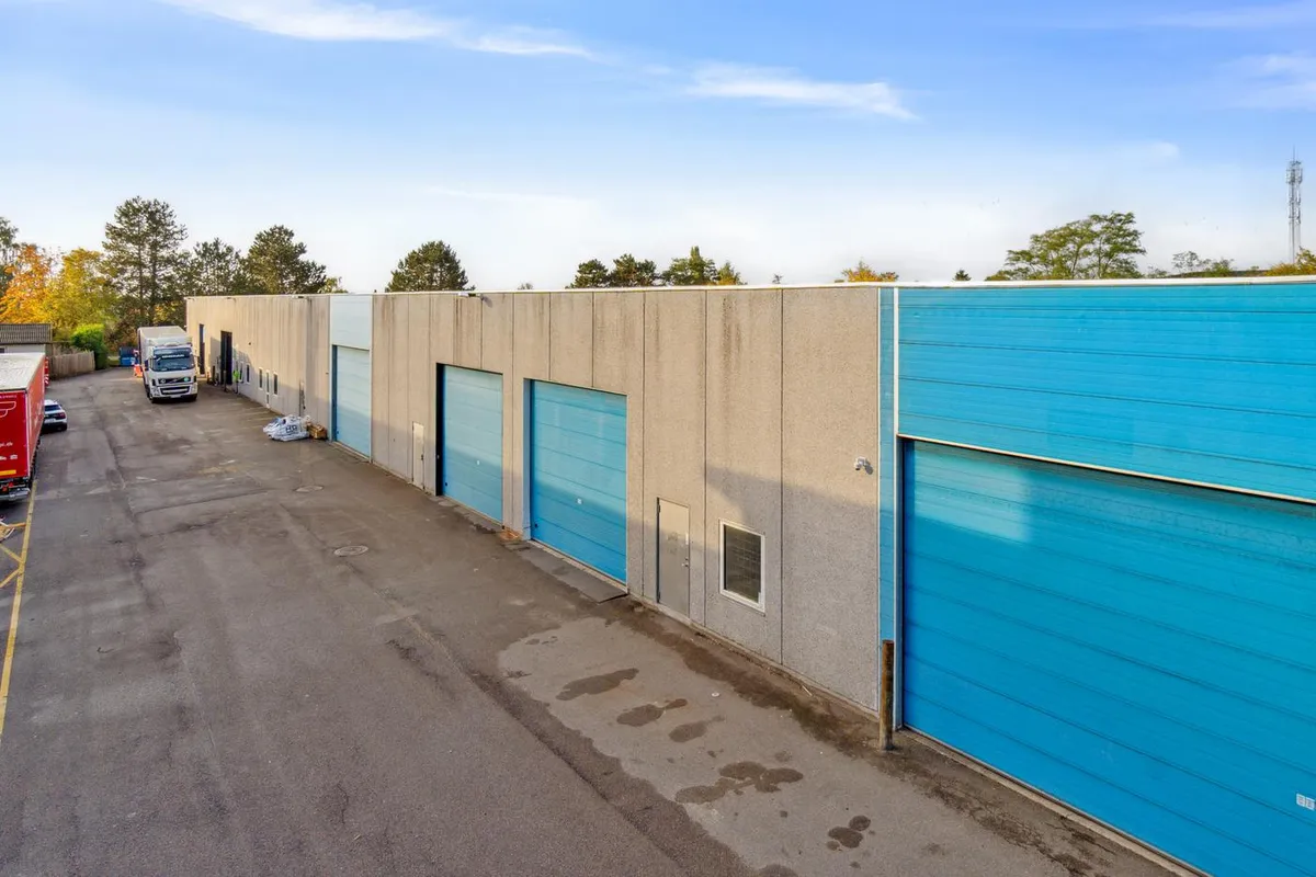 Et stort lager med blå garageporte og en lastbil, der kører ud af garagen og en anden lastbil, der står parkeret