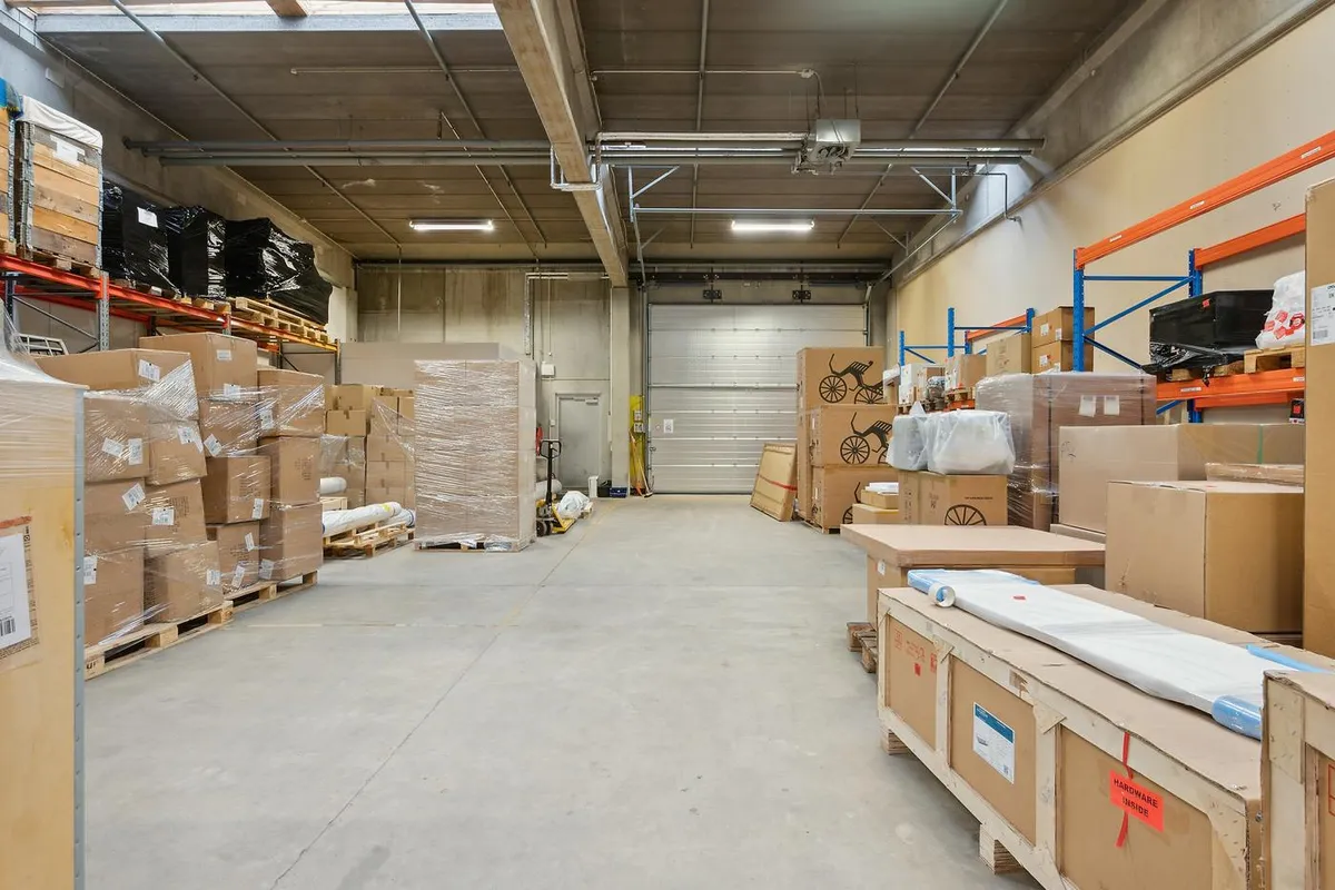 Lager med store og små kasser og pakker i en stor bygning, hvor der er stående hylder med kasser