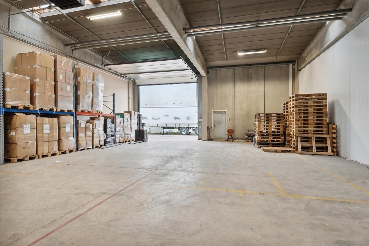 En stor lagerhal med en stor åbning til lastbiler og flere paller med emballage og lagervarer