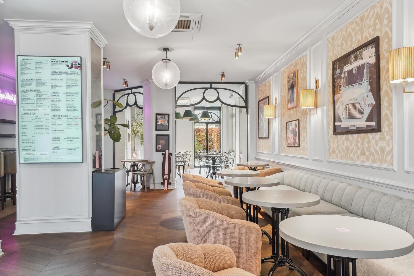 Moderne restaurant med lyse loftslamper, runde borde, lyse puder og en digital menuvæg på højre side