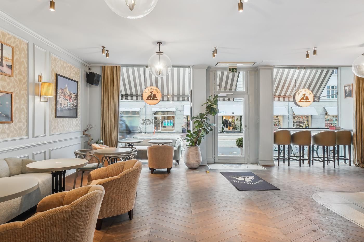 Lejemål med store vinduer og lyse loftslamper samt møbler og plante i midten og stolpe og skilt på gulvet