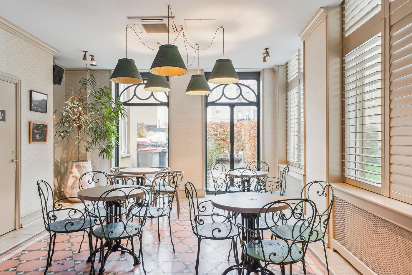 Indvendørs café med møbler og lamper i loftet, vinduer med jalousier og en stor plante