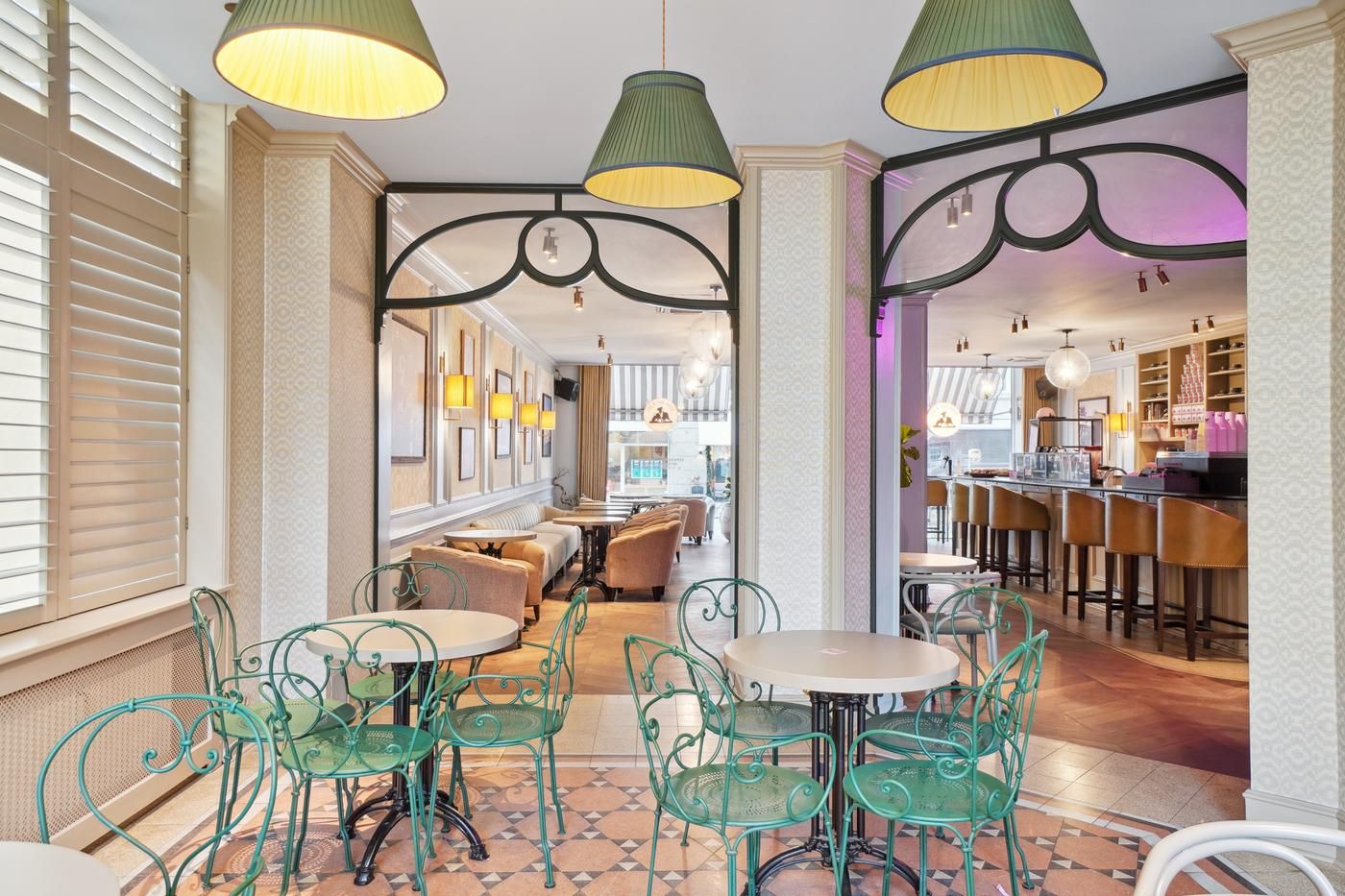 En hyggeligt indrettet café med lyse og elegante stole, højt oplyste lamper og en åben dør til bagværkshylder