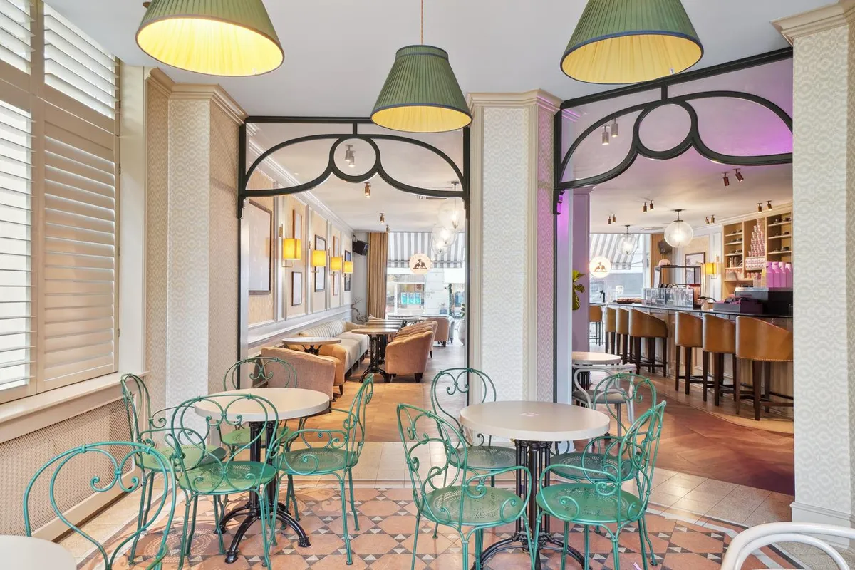 En hyggeligt indrettet café med lyse og elegante stole, højt oplyste lamper og en åben dør til bagværkshylder