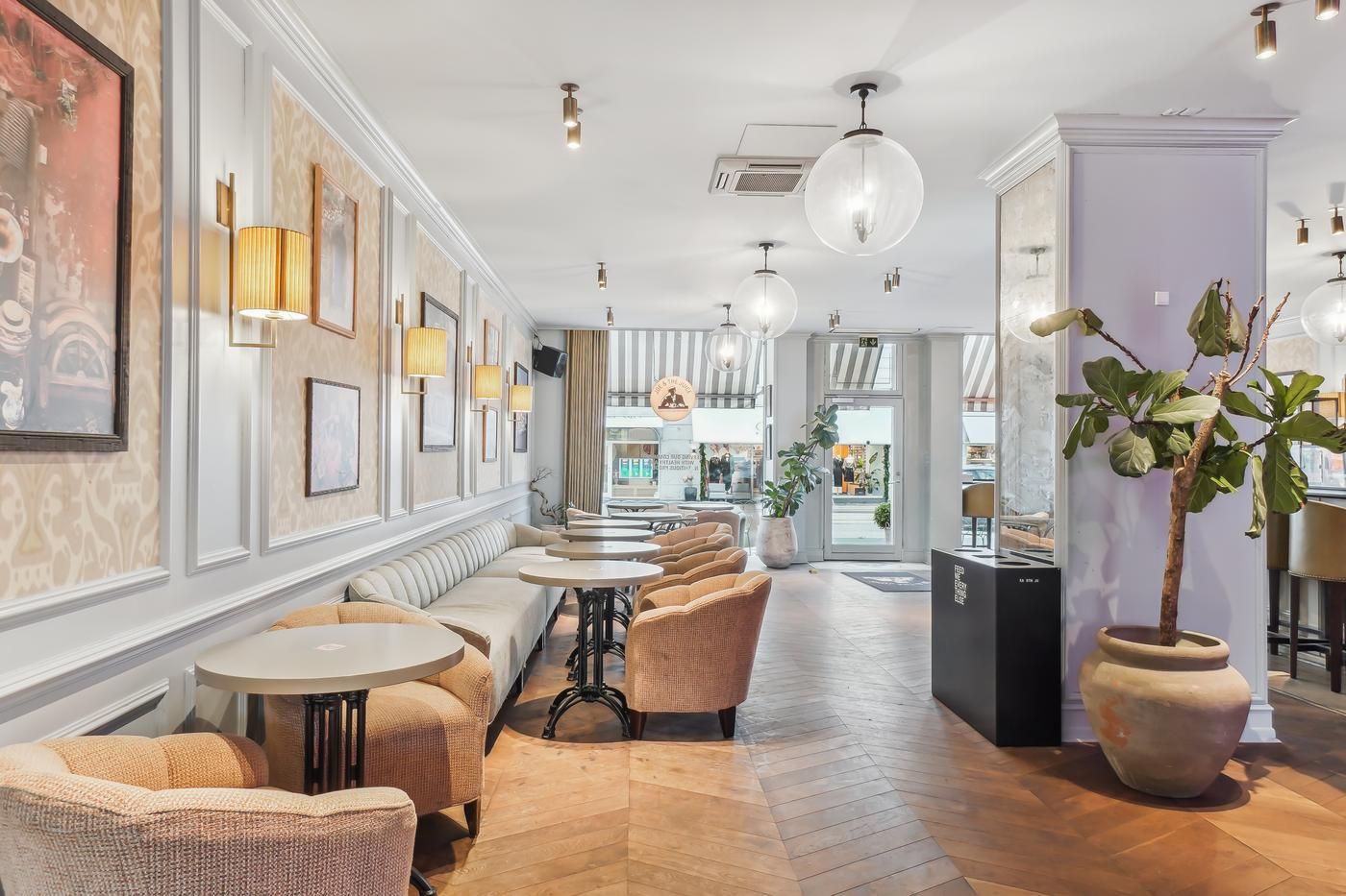 Inde i en café med lyse lysekroner, lyse borde og stole, plante i stor jordkugle og billeder på væggen