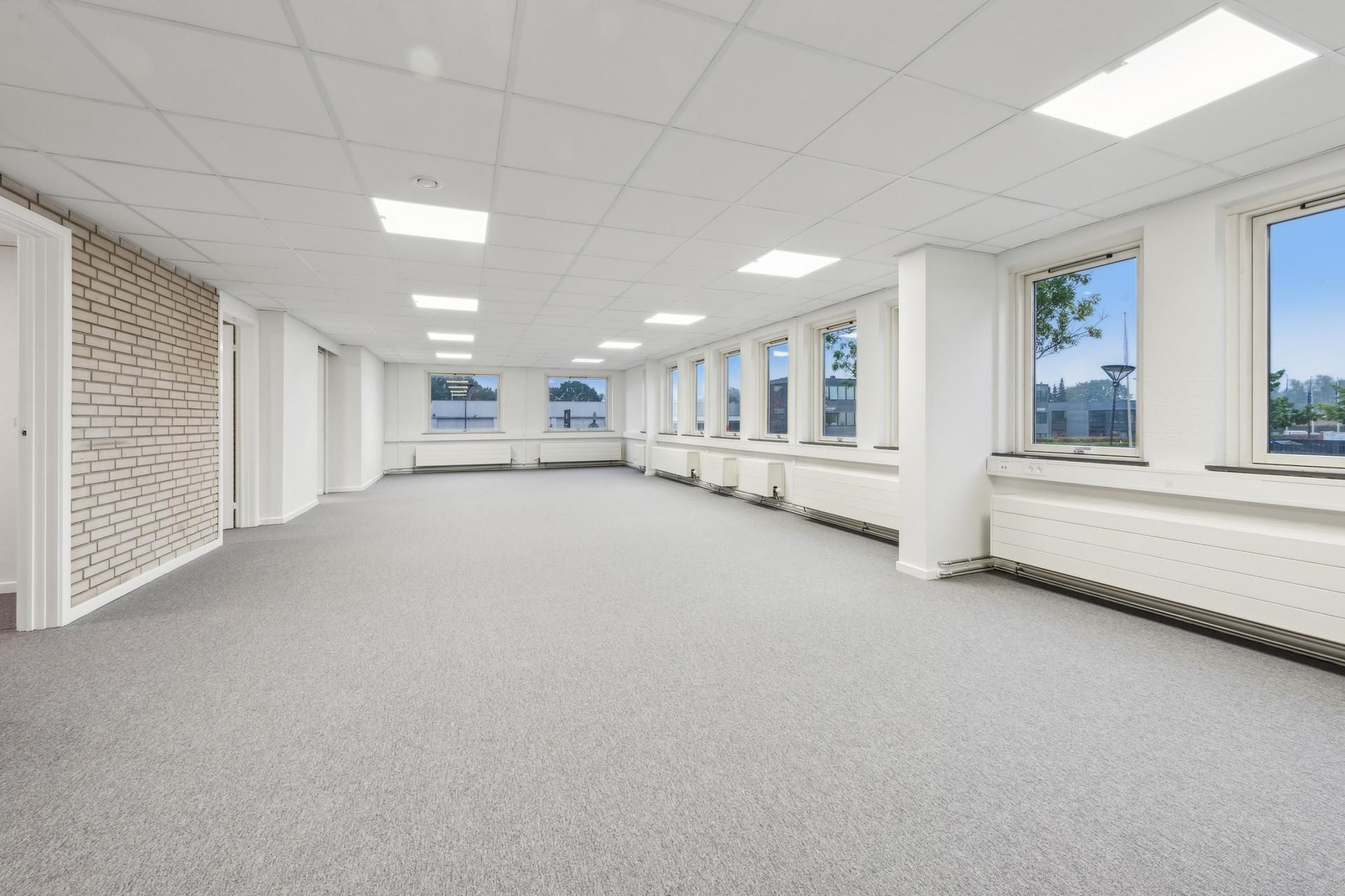 Et stort, lyse og moderne kontor med hvide vægge, loft og gulv samt flere store vinduer og lyse lyskappe i loftet