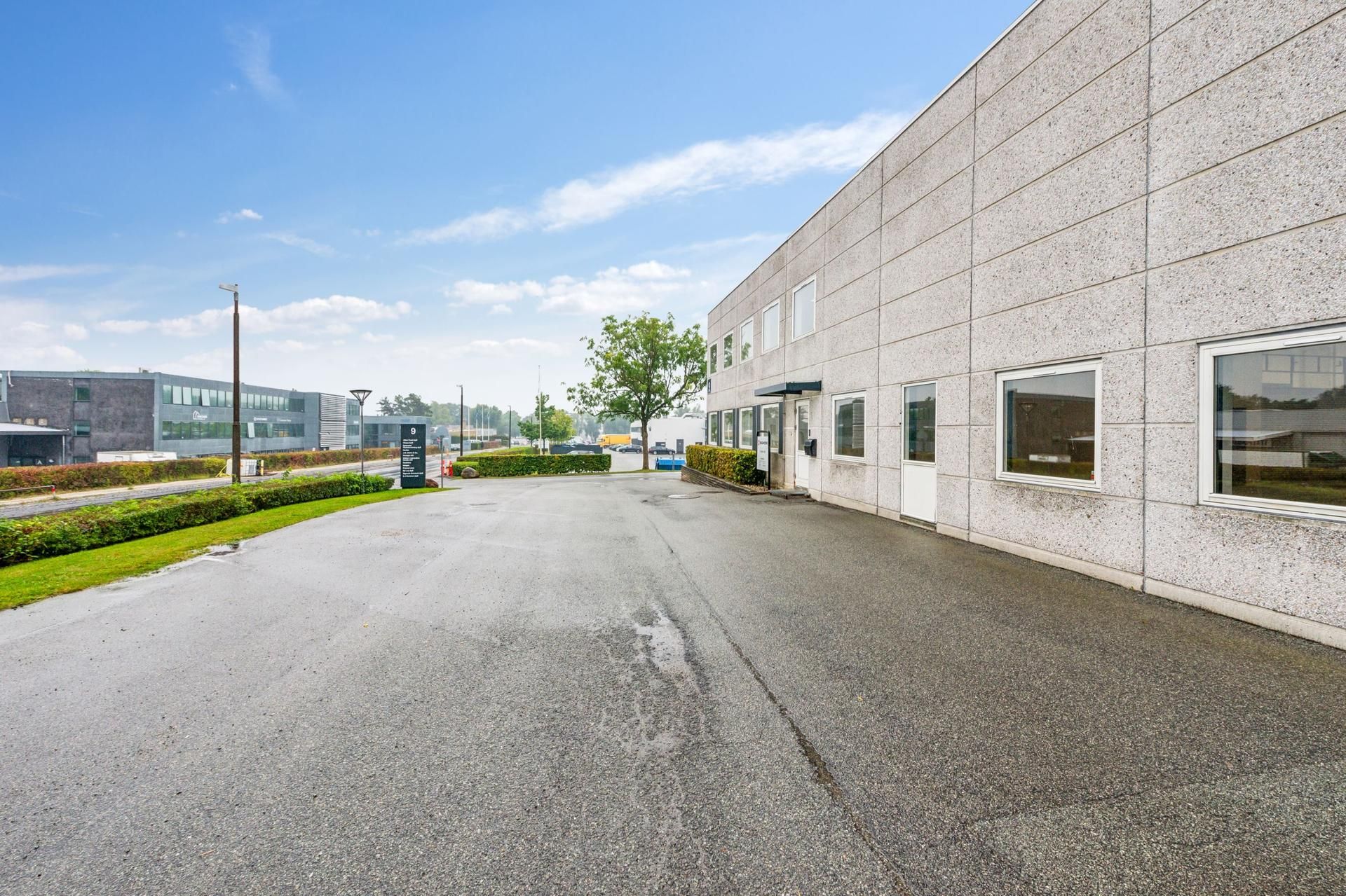 Vej og forhøjede sider med buske og planter og bygninger i baggrunden