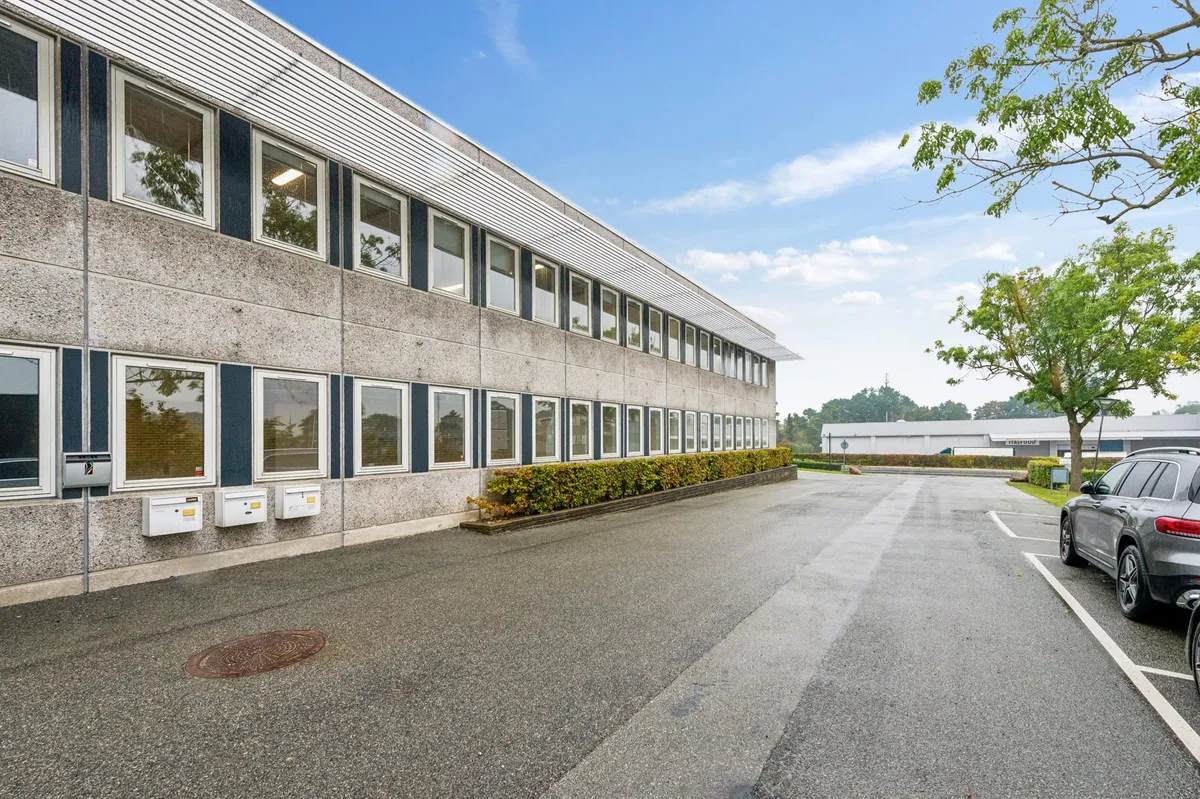 Kontorbygning med store vinduer og højt til loftet, placeret ved siden af en parkeringsplads med en suv parkeret