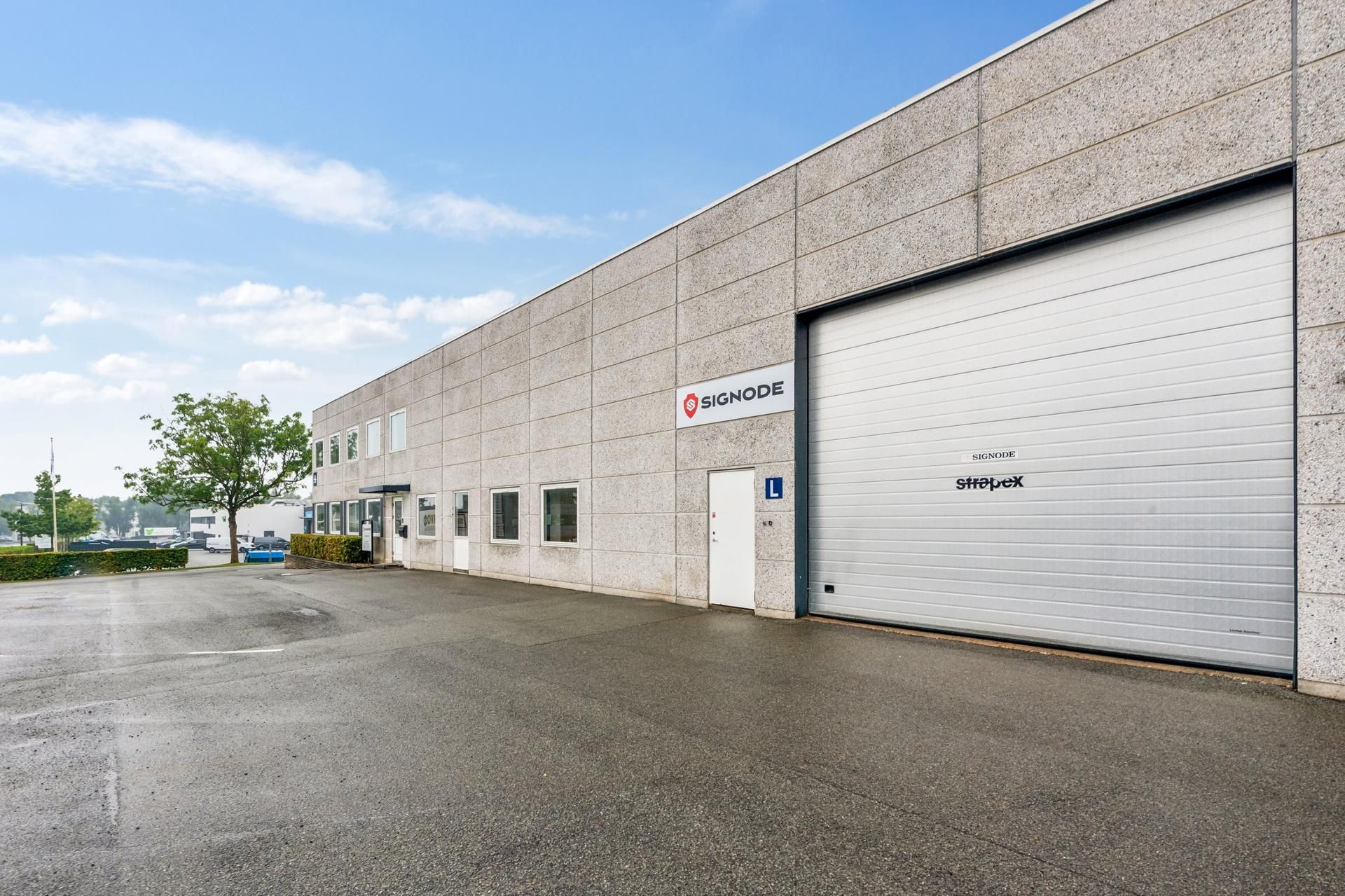 Lagerbygning med store garagedøre, flere indgange, Signode-logo og Stratex-skrifttræk i væggen, uden folk eller køretøjer i