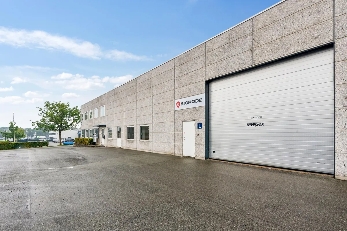 Lagerbygning med store garagedøre, flere indgange, Signode-logo og Stratex-skrifttræk i væggen, uden folk eller køretøjer i