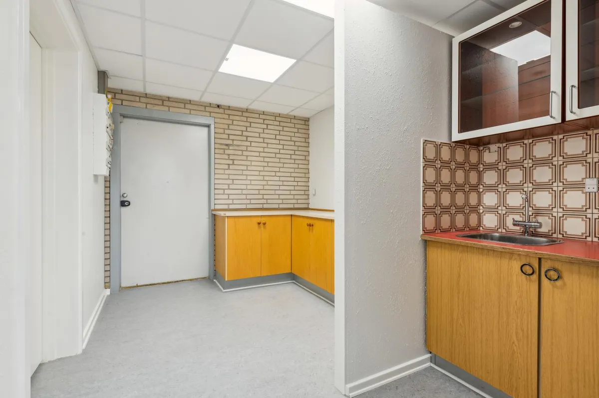 En stor, lys og tom lagerlokal med gulv, hvidt loft, gule vægge og røde bordplade med vask og spejlskabe