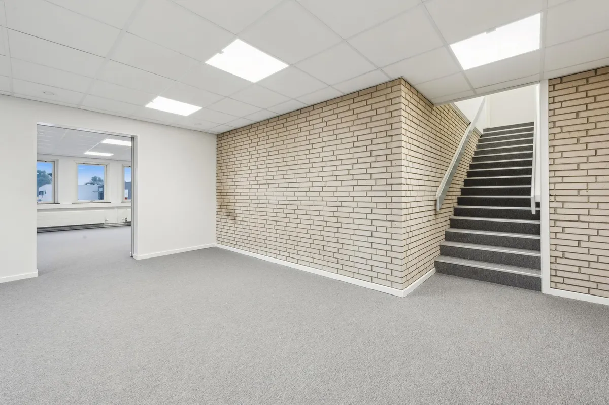 Rummelige lokaler med højt til loftet og lyse vinduer, indrammet af hvide vægge og gulve. Trapper med grå forstærkning fører