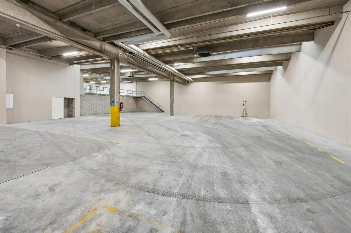 Lager med store, høje lofter og åbne pladser, der er ideelt til lagerplads og kontorer, udstyret med lyse loftslampe, hvide