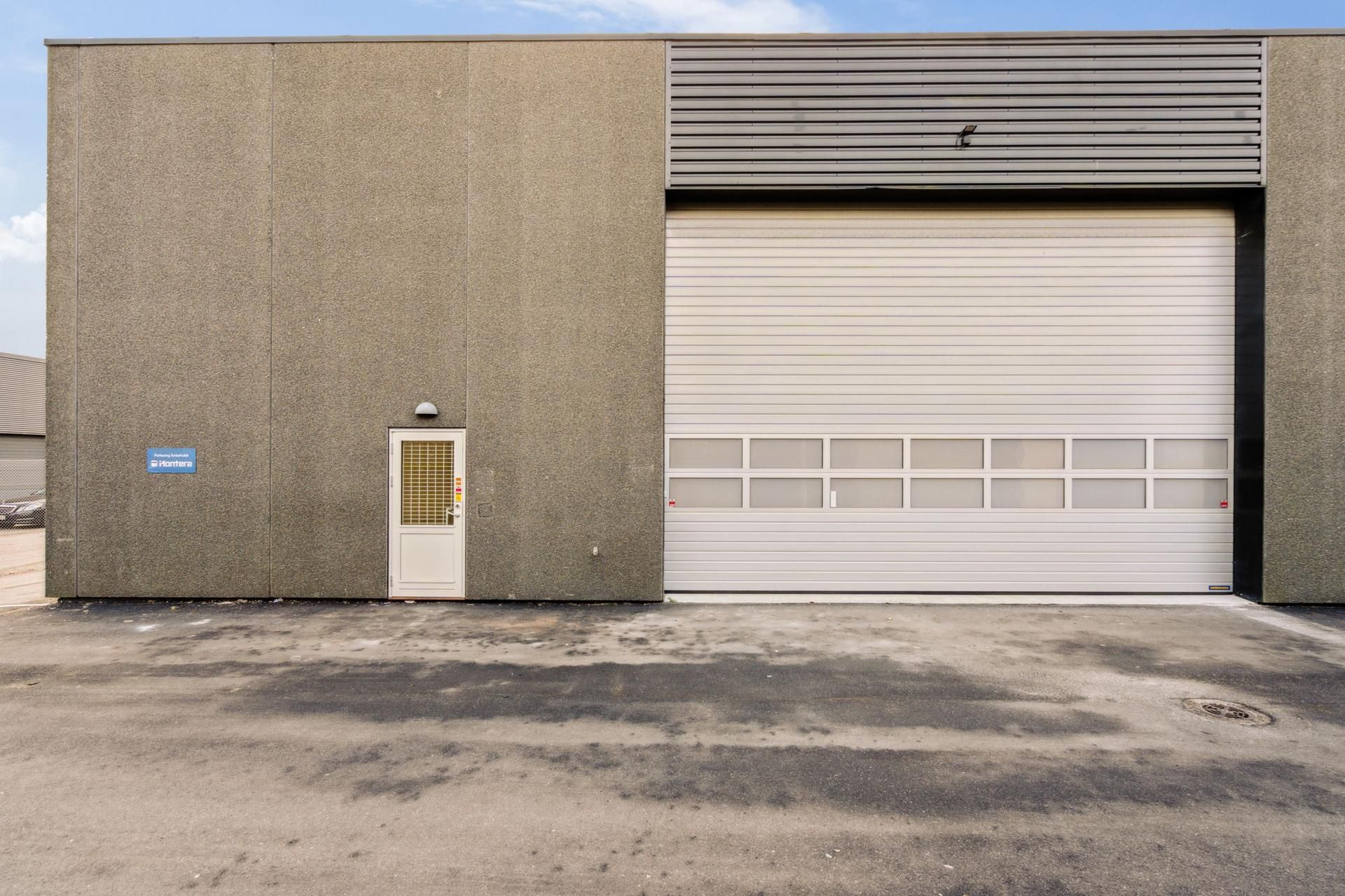 Foto af et lejemålsobjekt med en hvid garagedør, et hvidt sidedør og et skilt med teksten Parking Sabathiel & Hammera