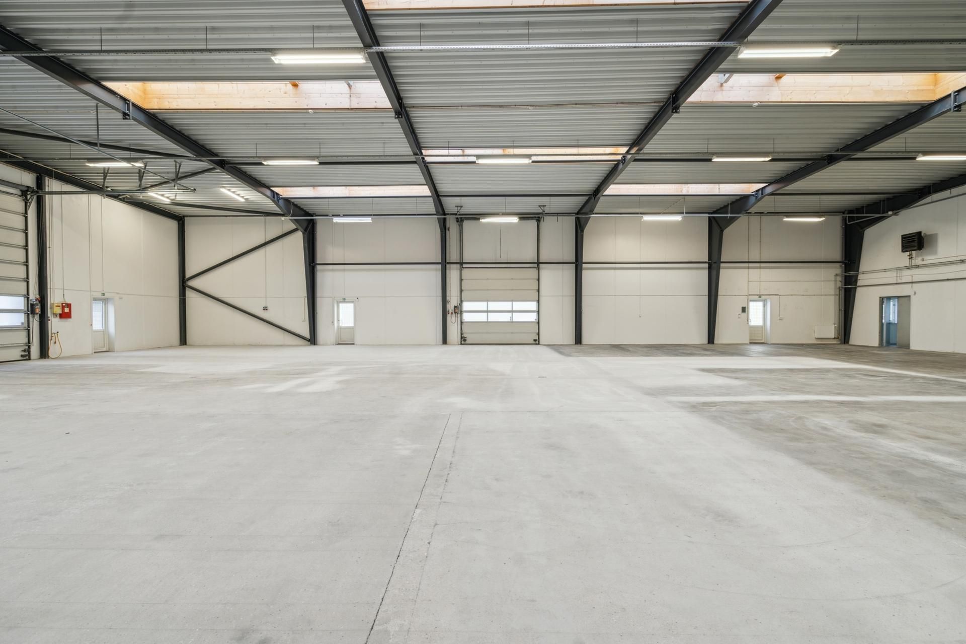 En stor, hvid, industriel lagerhal med højt loft og fire større garagedøre. Væggene er isolerede og der er flere store