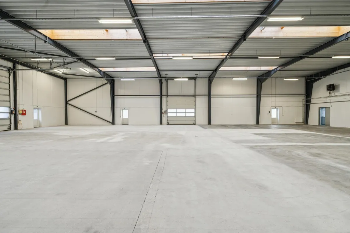 En stor, hvid, industriel lagerhal med højt loft og fire større garagedøre. Væggene er isolerede og der er flere store
