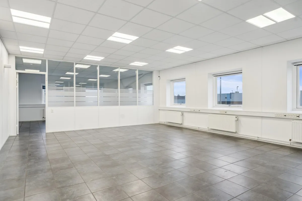En stor, mørkt grå fliserede gulv og vægge i et tomt kontor med tre vinduer og tre radiatorer.