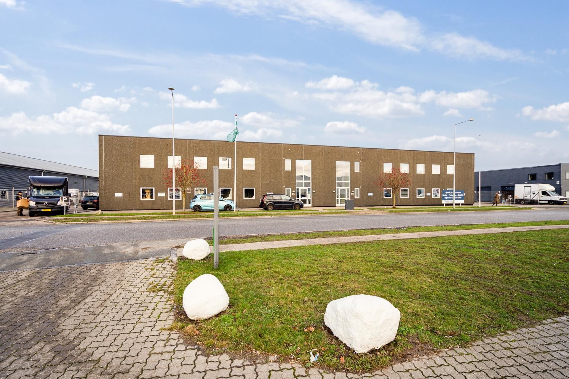 Et lagerhus med flere vinduer og to biler parkeret udenfor under en skyet himmel