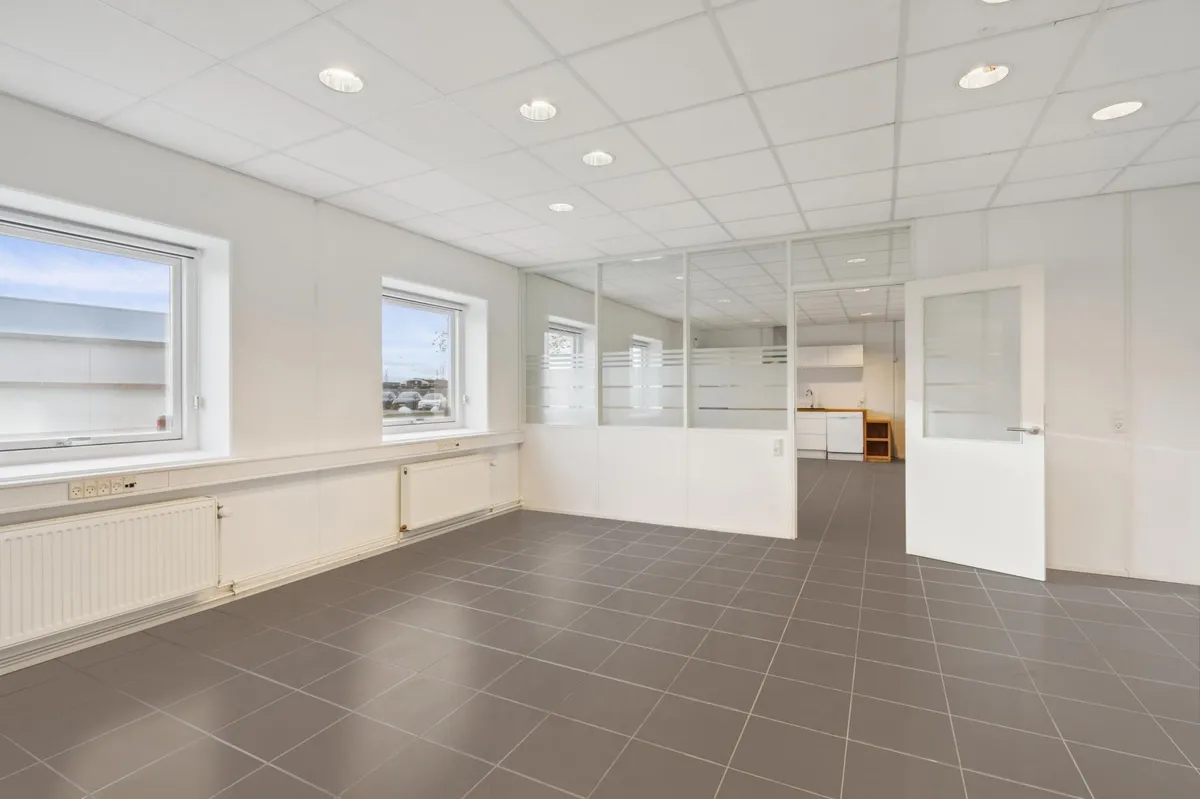 Et tomt, lyserødt rum med vinduer og indgangsdør, hvor væggene er hvide og gulvet er gråt