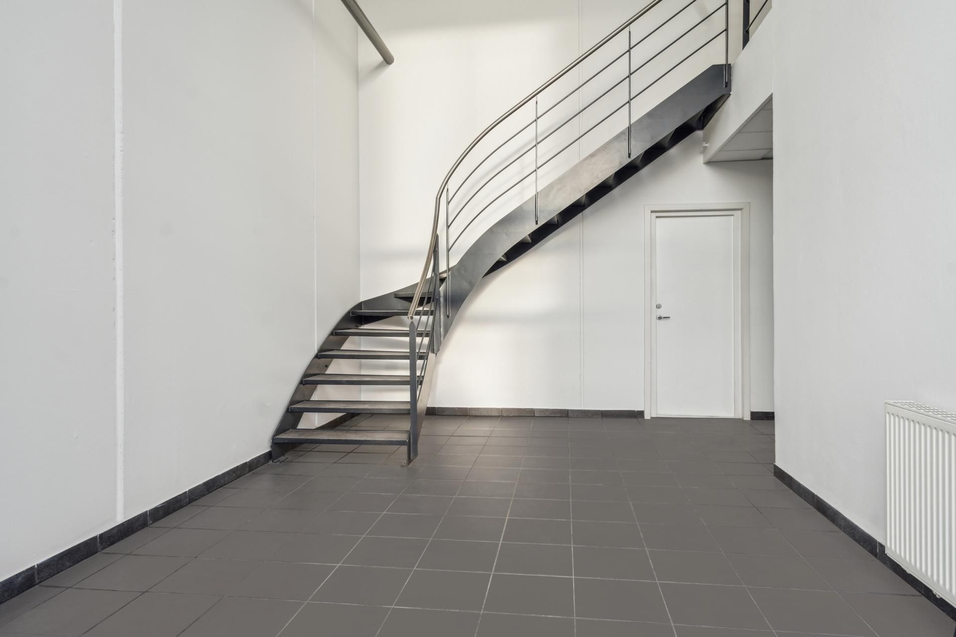 Rummelig, minimalistisk og moderne kontorlokal med åben stue, trappe og lyse gulvfliser.