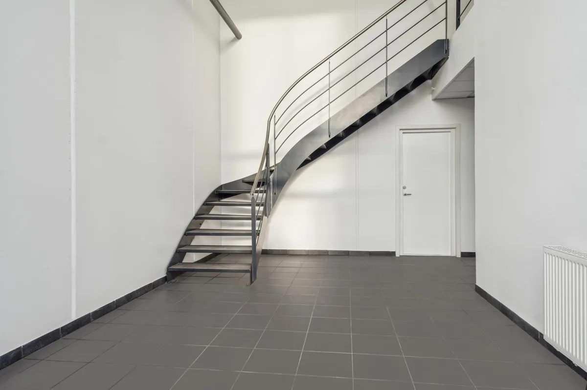Rummelig, minimalistisk og moderne kontorlokal med åben stue, trappe og lyse gulvfliser.